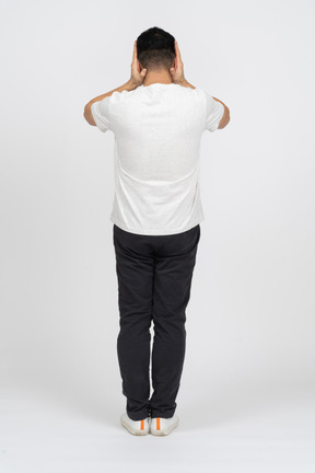 Vista traseira de um homem em roupas casuais, cobrindo os ouvidos com as mãos