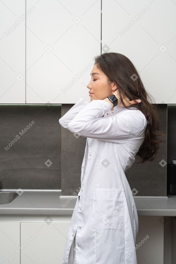 Side view of a female doctor touching her neck with her eyes closed
