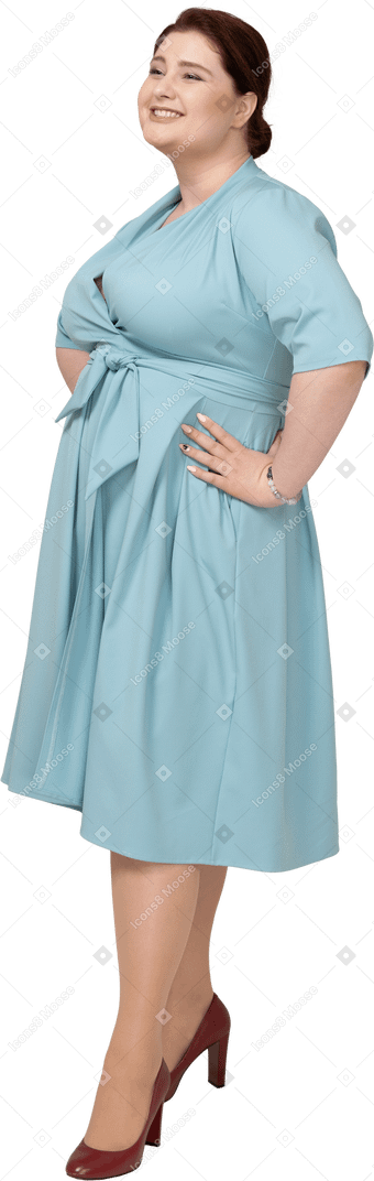 Vorderansicht einer glücklichen frau im blauen kleid, die mit den händen auf den hüften steht