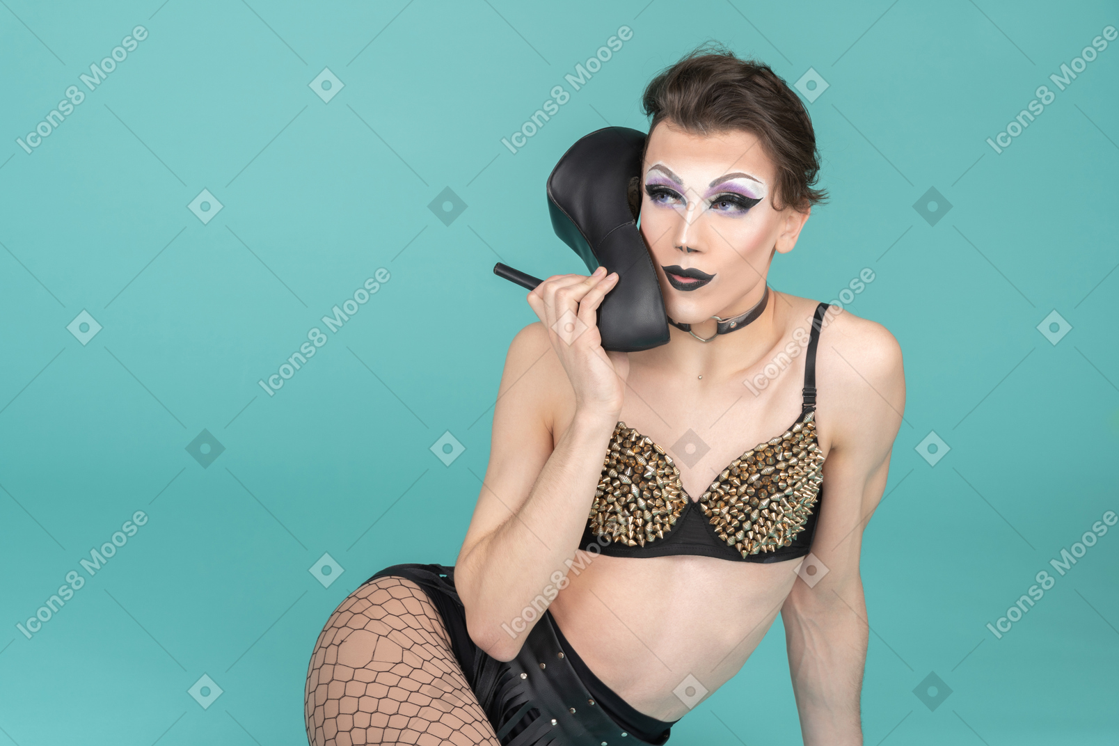 Drag queen in studded bra using shoes as phone