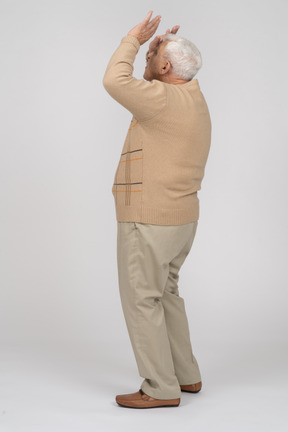 Vista laterale di un vecchio in abiti casual in piedi con le mani alzate e alzando lo sguardo