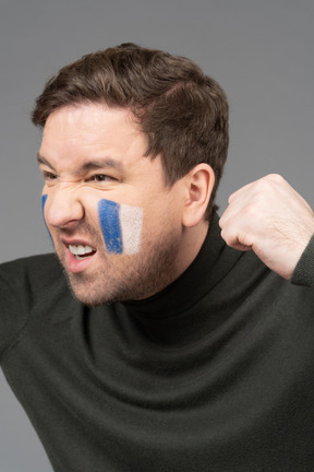 O retrato de um fã de futebol masculino com o rosto em branco e azul cerrando os punhos