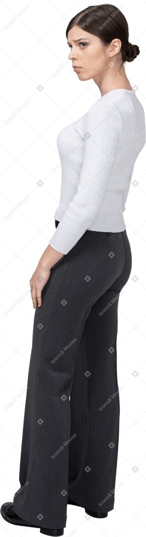Three-quarter back view of a young woman in office clothing standing still & knitting brows