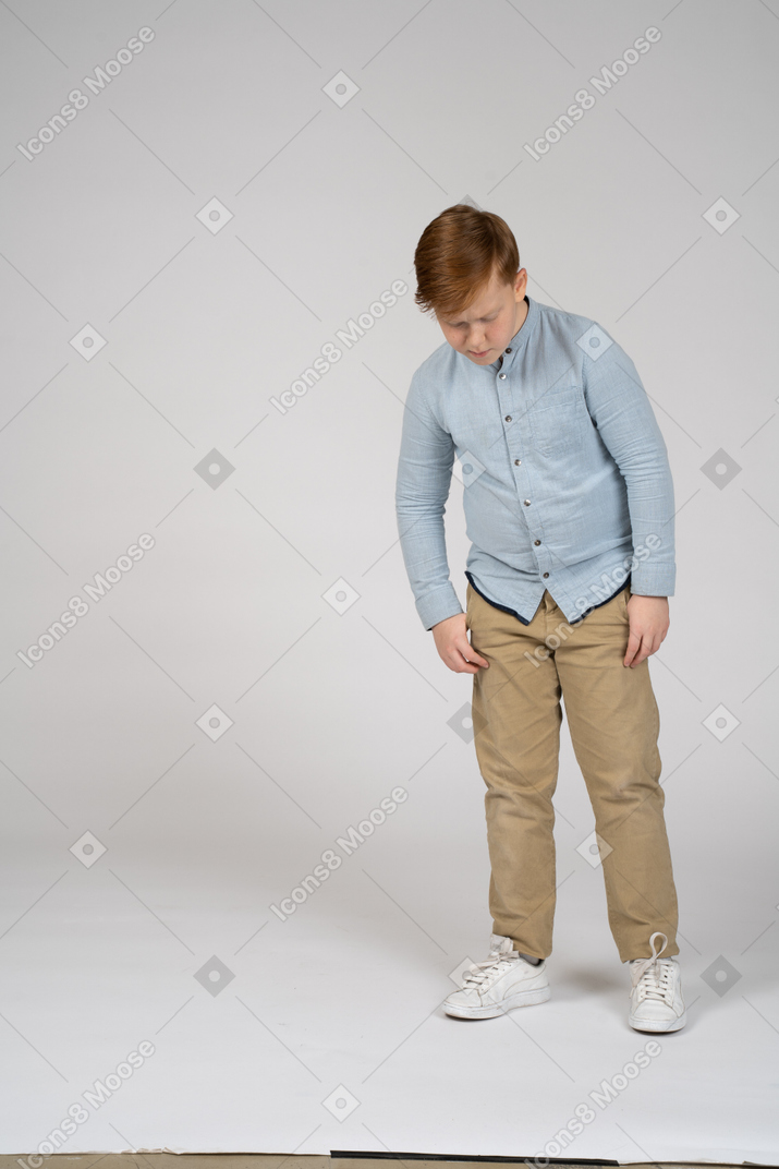 Niño con camisa azul de pie y mirando hacia abajo