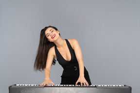 Front view of a pleased young lady in black dress playing the piano while smiling