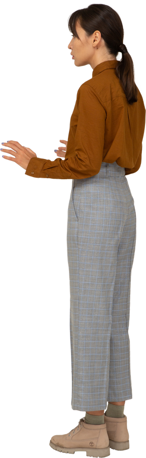 Vista posterior de tres cuartos de una joven mujer asiática en calzones y blusa levantando sus manos