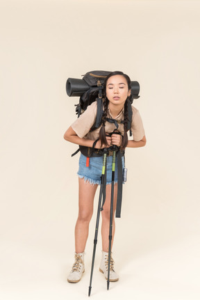 Tired young hiker woman standing with huge backpack and leaning on trekking poles