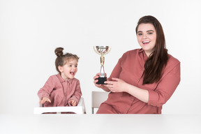 Mother and her little daughter sitting at the table with an award cup