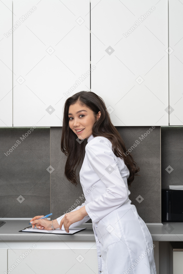 Side view of a smiling female doctor taking notes on her tablet and looking at camera