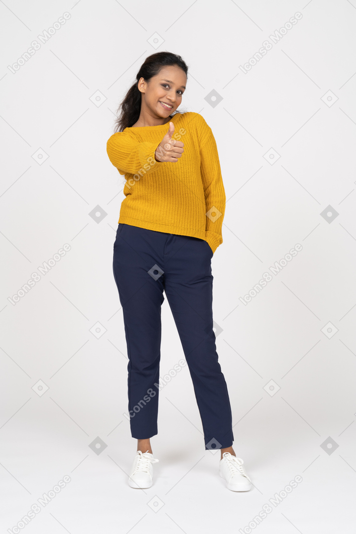 Front view of a happy girl in casual clothes showing thumb up and looking at camera