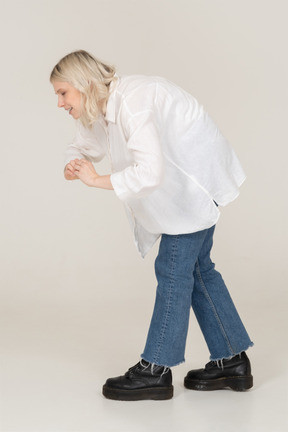 Vista lateral de uma mulher loira em roupas casuais, mostrando um gesto de coração ao se dobrar