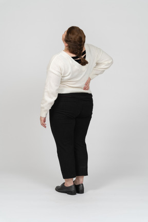 Rear view of plump woman in white sweater suffering from pain in lower back