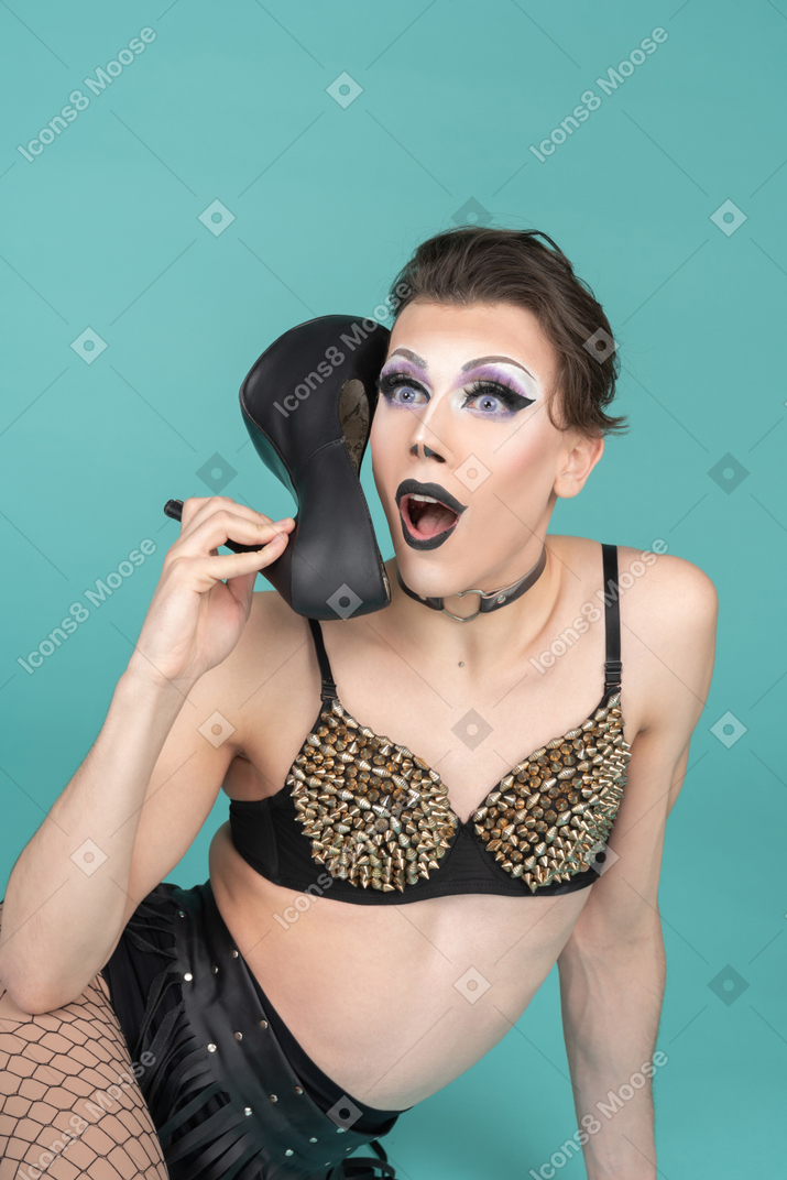 Drag queen in studded bra talking on the shoe