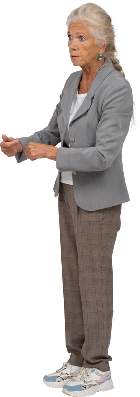 Вид сбоку впечатленной старушки в костюме, стоящей со сжатыми кулаками