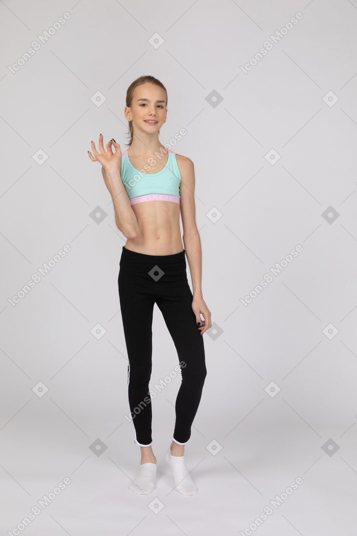 Веселая девочка-подросток в спортивной одежде показывает знак ок