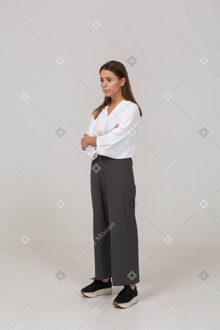Three-quarter view of a displeased young lady in office clothing crossing arms