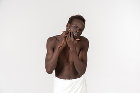 A young black man with a white bath towel around his waist doing his morning routine