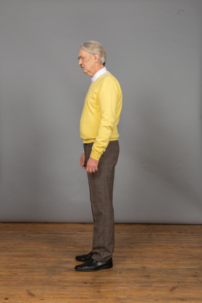 그의 눈을 감고 여전히 서있는 노란색 스웨터에 슬픈 노인의 측면보기