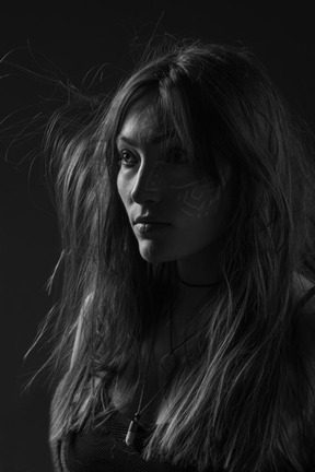 Noir three-quarter portrait of a young female with ethnic facial art and messy hair