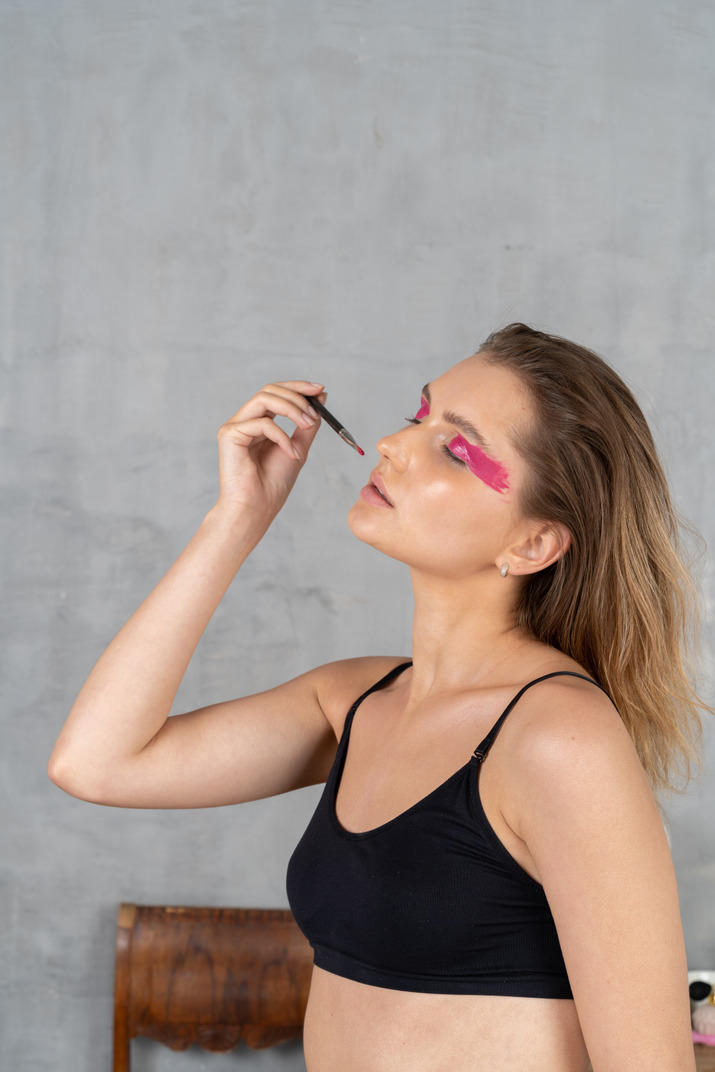 Three-quarter view of a young woman with bright pink eye make-up holding brush