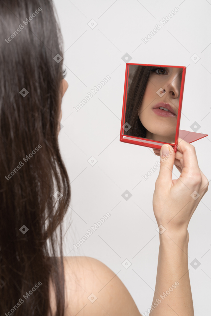 Pretty female looking at red hand mirror