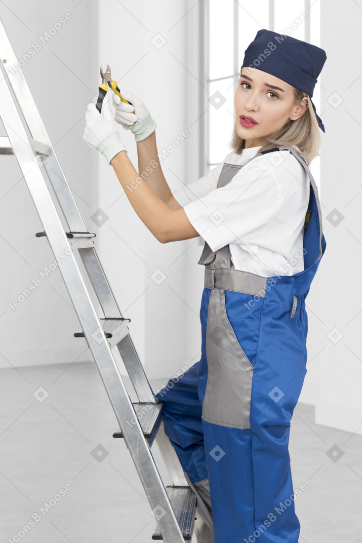 Woman standing on a ladder holding pliers