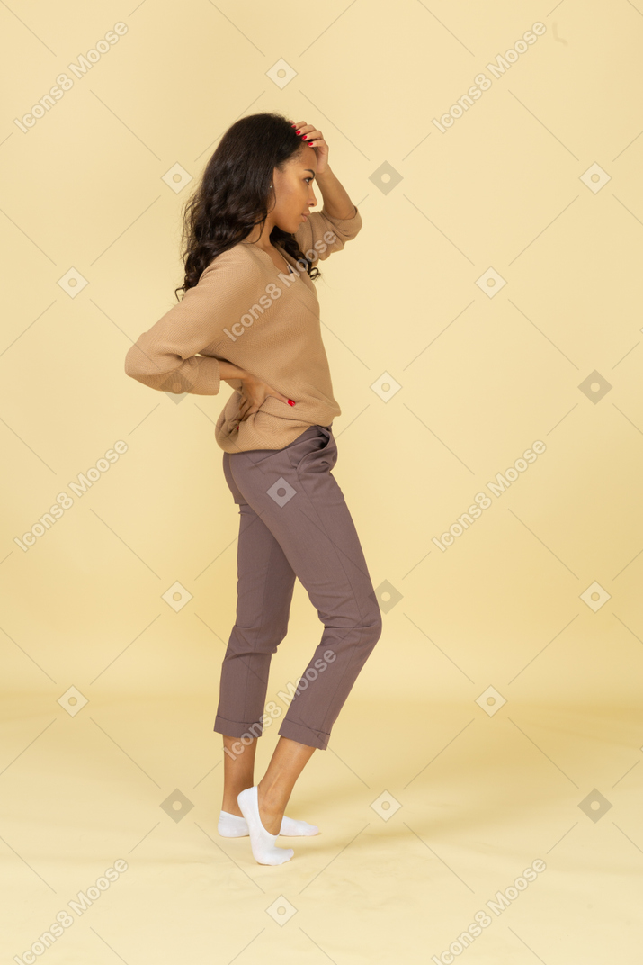 Side view of a dark-skinned young female putting hand on hip while touching head