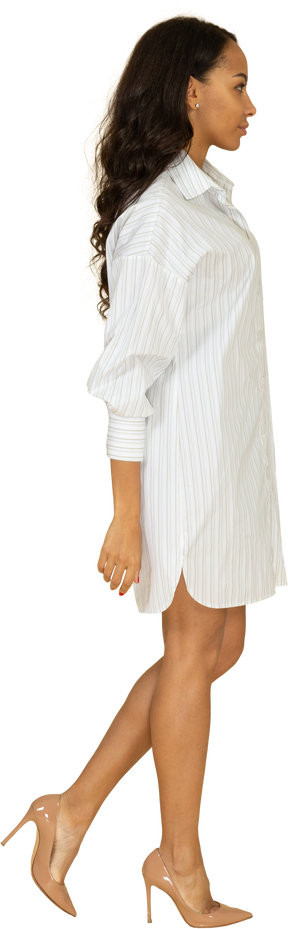 Vista lateral de una mujer joven de piel oscura caminando confiada en vestido blanco