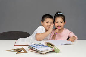 Irmão e irmã sorrindo enquanto fazem lição de casa