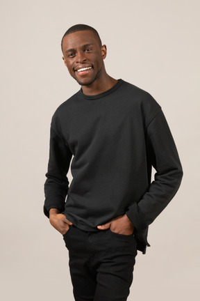 Young smiling man keeping hands in pockets and looking at camera