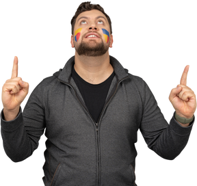 Front view of a male football fan with colorful face art raising fingers