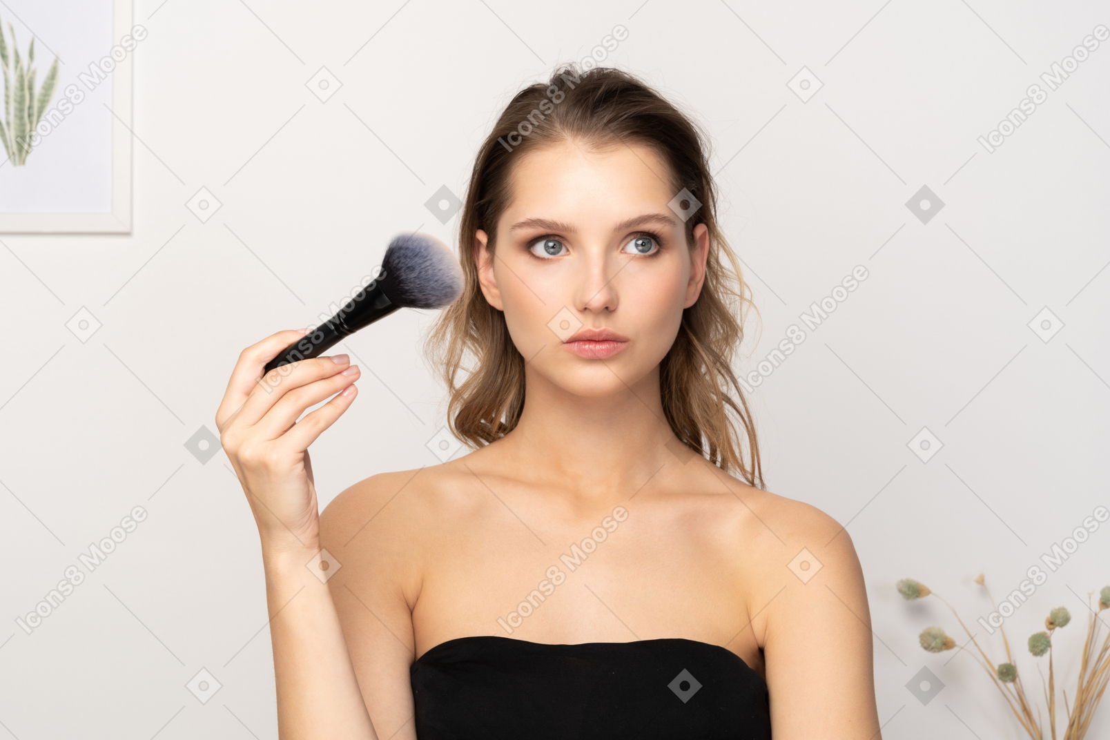 Vista frontal de una mujer joven sensual pensativa sosteniendo un pincel de maquillaje