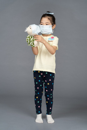 Portrait of a little girl and her toy wearing face masks