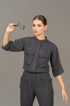 Front view of young woman in a jumpsuit holding a magnifying glass