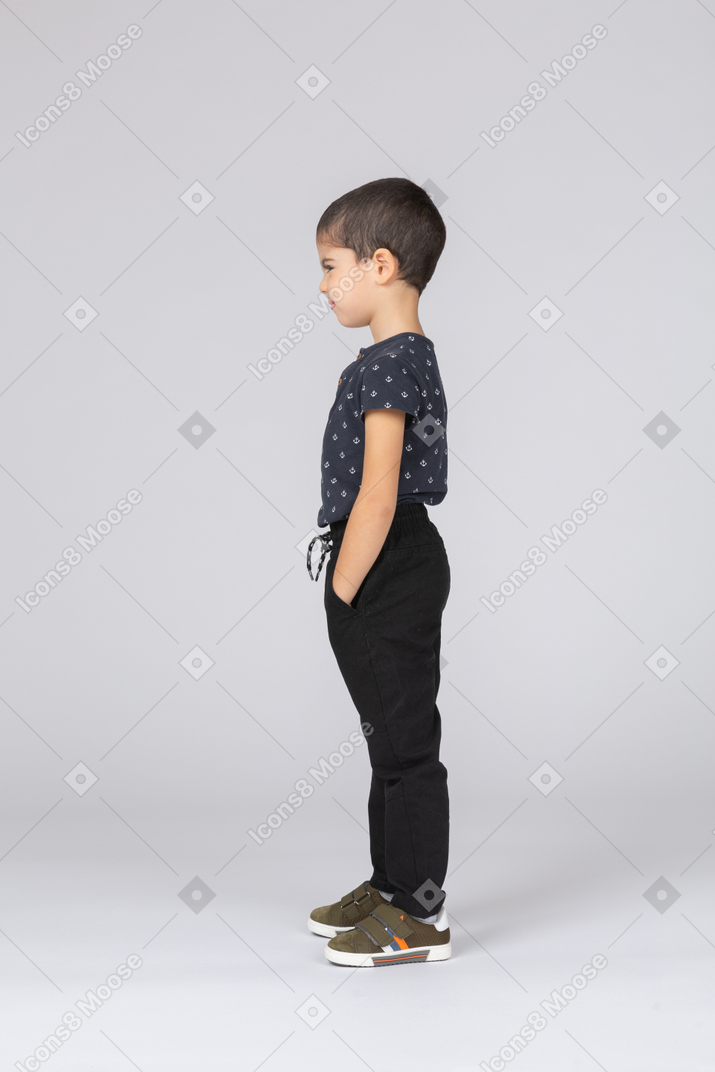Side view of a cute boy in casual clothes posing with hands in pockets