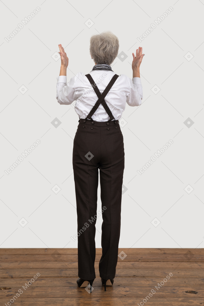 Вид сзади пожилой женщины в офисной одежде, поднимающей руки