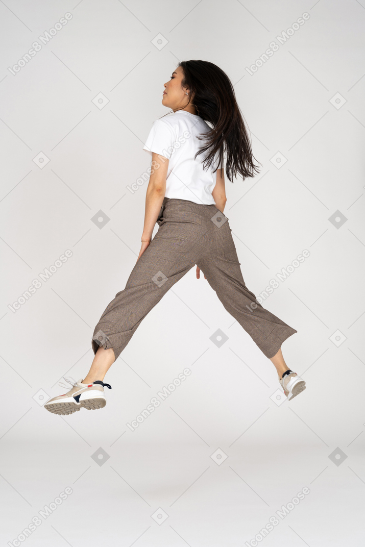 Вид сзади прыгающей молодой леди в бриджах и футболке, раскинувшей ноги