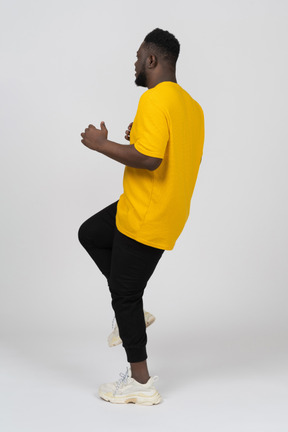 脚を上げる黄色のtシャツを着た若い浅黒い肌の男の側面図