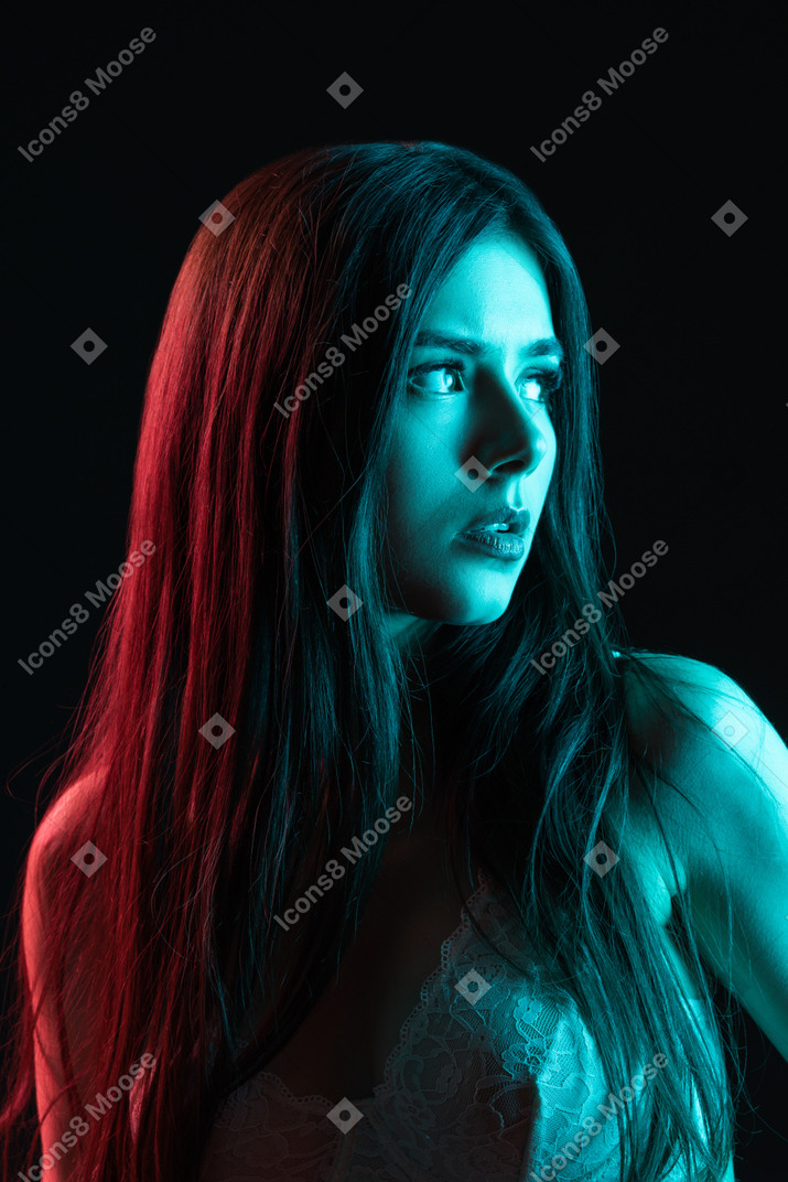 Молодая женщина в бюстгальтере смотрит в сторону в синем неоновом свете