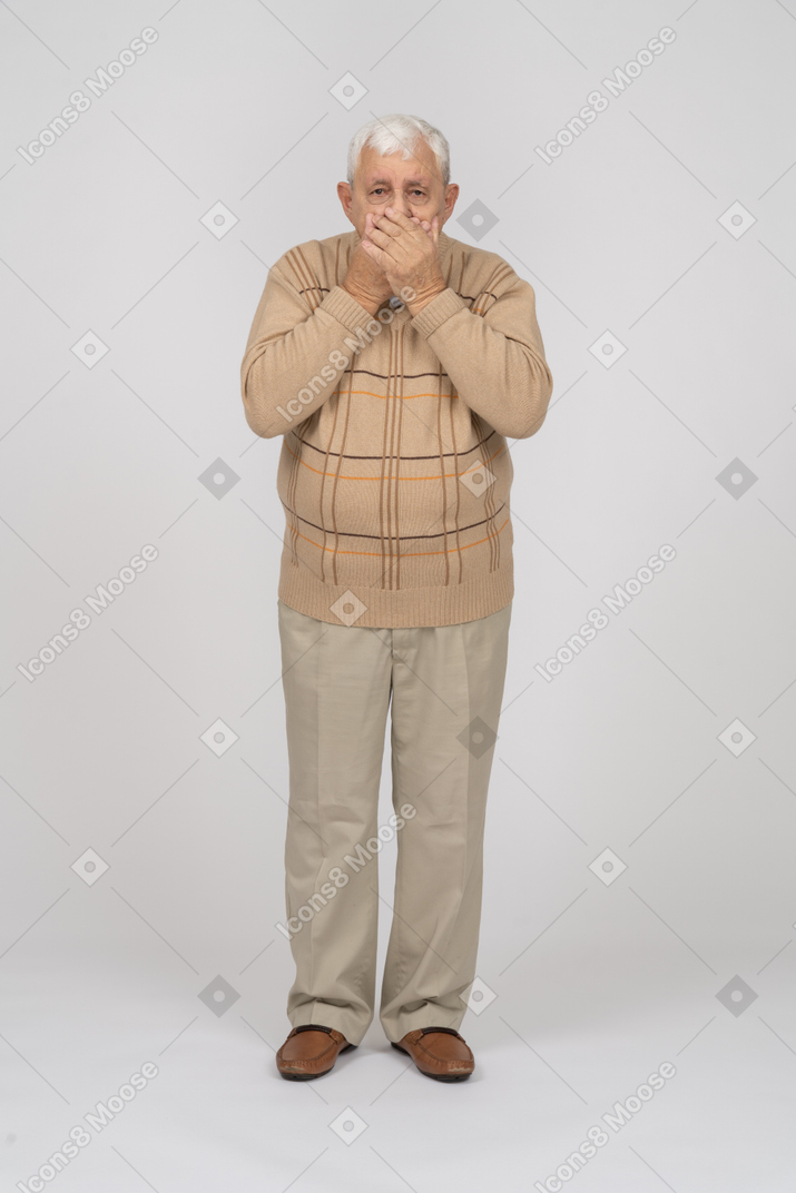 Front view of a scared old man in casual clothes covering mouth with hands