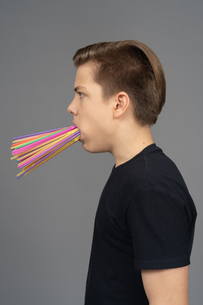 Side portrait of young male holding plastic straws in his mouth