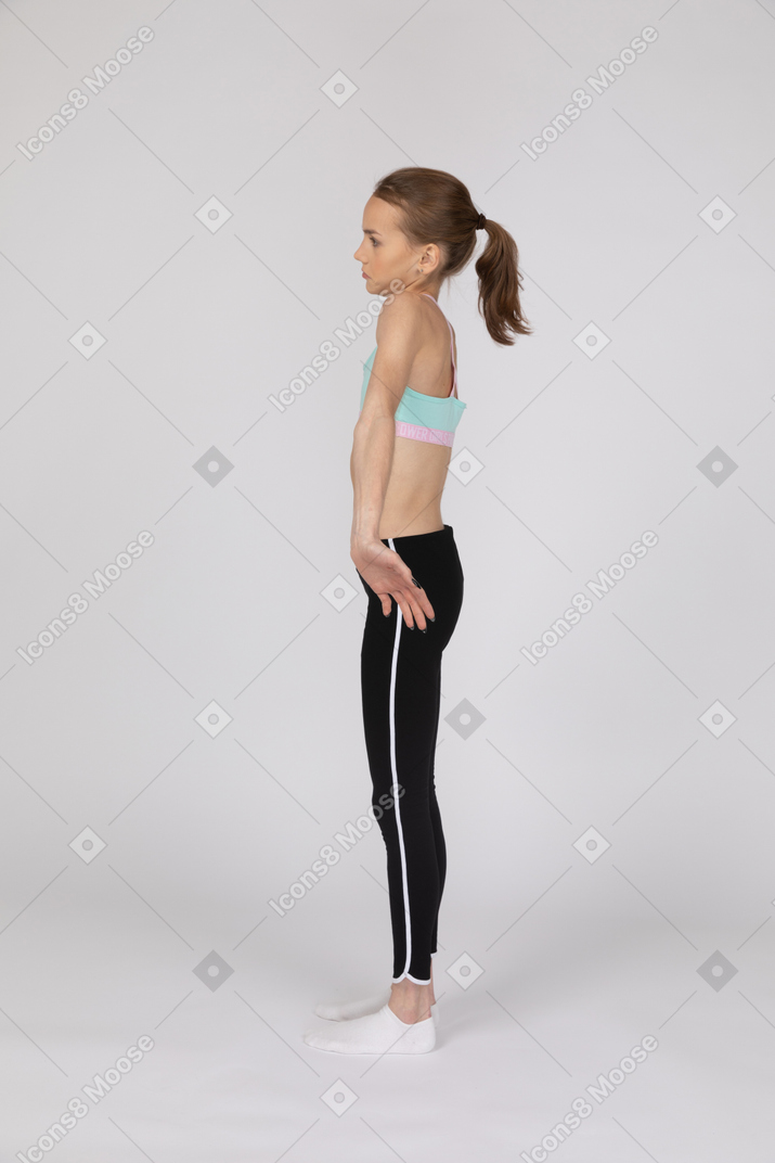 Vista lateral de una chica confundida de pie con los brazos abiertos.