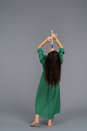 Back view of a young lady in green dress playing flute while leaning back