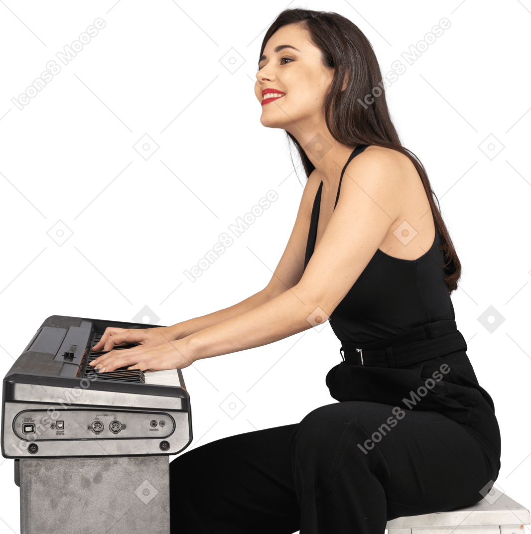 Vue latérale d'une jeune femme assise souriante en costume noir à jouer du piano