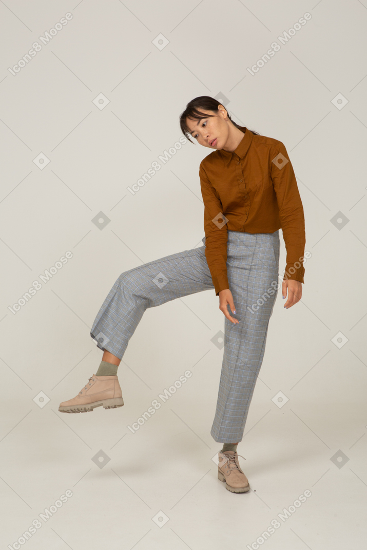 Vista frontal de uma jovem mulher asiática de calça e blusa levantando a perna