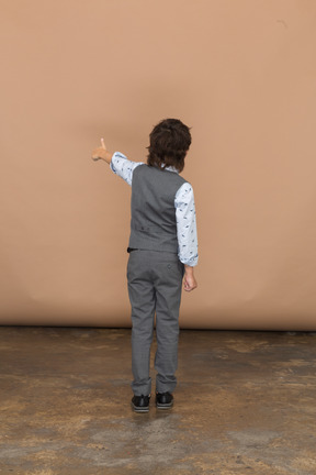 Вид сзади на мальчика в сером костюме, показывающего большой палец вверх