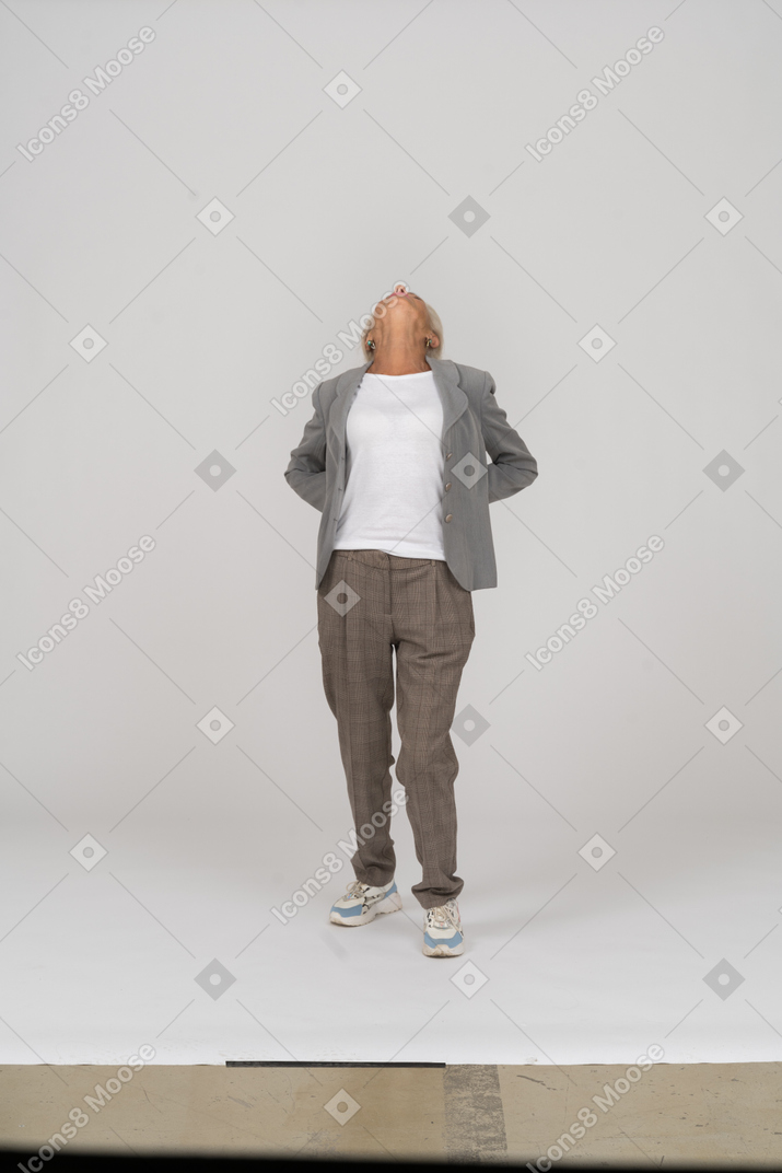 Vista frontal de una anciana en traje de pie con las manos detrás de la espalda y mirando hacia arriba