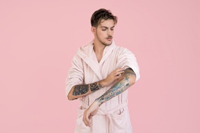 Handsome young in pink robe looking at his hand