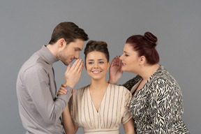 Young man and young woman gossiping in smiling woman's ears