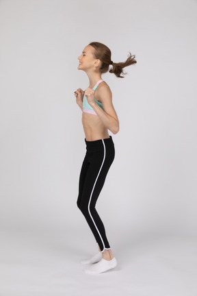 Vista lateral de uma adolescente alegre em roupas esportivas pulando